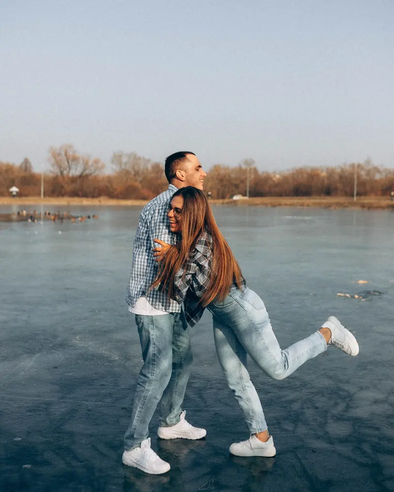Playful couple on a frozen lake, she kicks up a heel as he pulls her close.