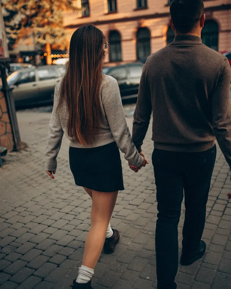 Back view of a couple walking hand in hand down a cobbled street.
