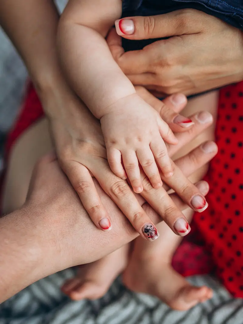 Detail of a baby's hand resting on the parents' hands.