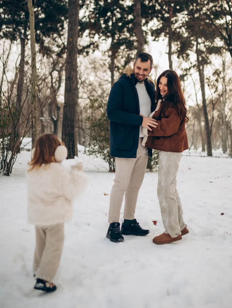 Winter family walk in a snowy Budapest park, the toddler seen from behind in a fluffy white coat.