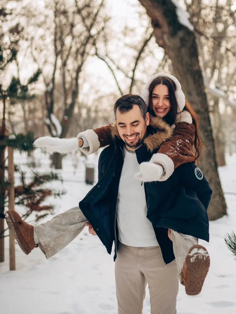 Dad gives mum a piggyback through the snow, both laughing.