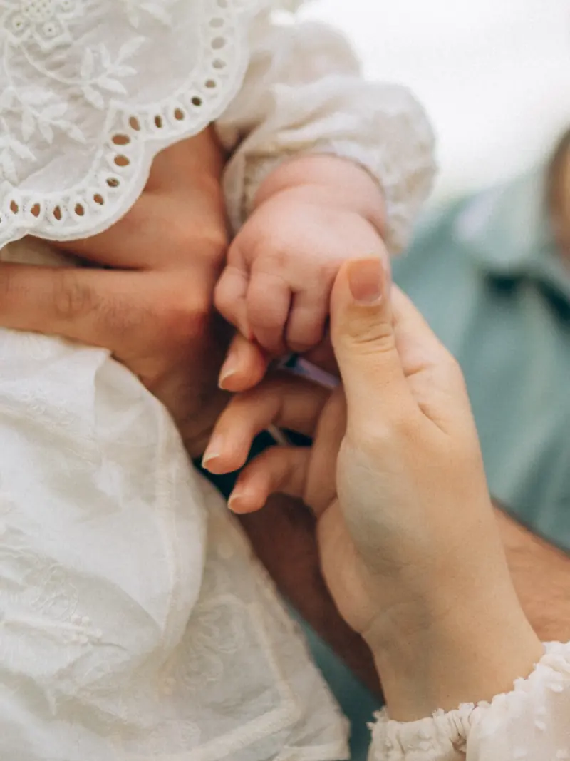 Detail of a baby's hand holding a parent's finger, white lace sleeves.