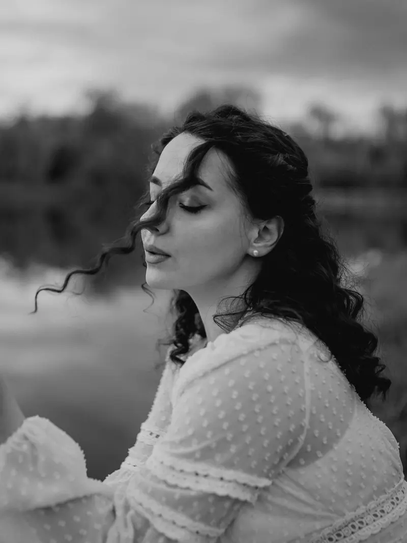 Black-and-white portrait of mum by the lake, her curls caught by the wind.