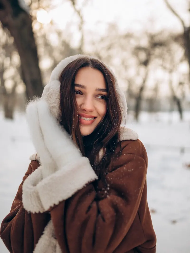 Mum smiling over her shoulder in a shearling coat in the snowy park.