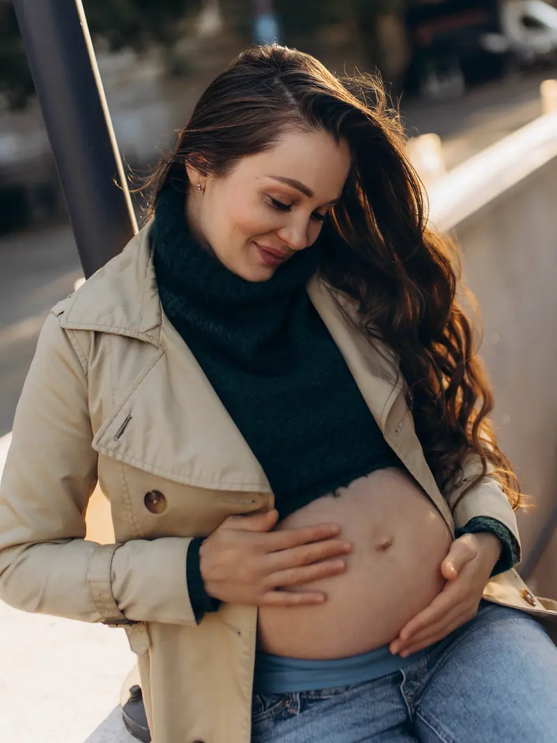 Soft warm detail of the mother looking down at her bump, hands cradling it.
