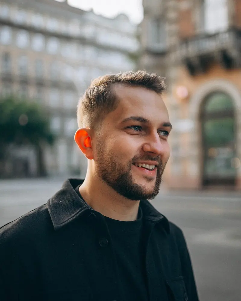 Smiling close-up of a man on Andrássy Avenue, the Opera softly blurred behind him.