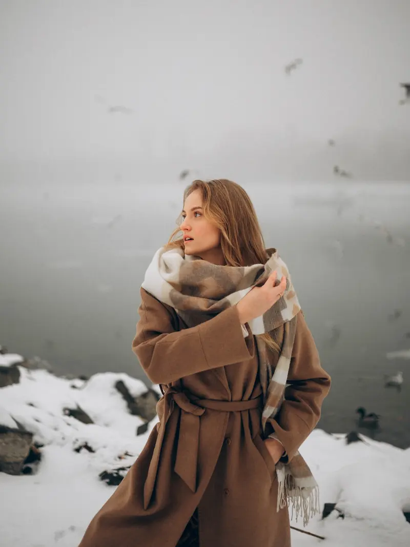 Full-length winter look on the snowy Danube bank, coat and scarf moving in the wind.