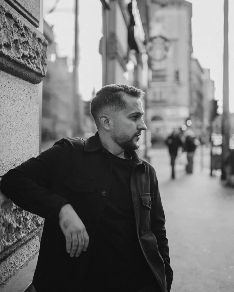 Black-and-white portrait of a man leaning on a pillar on a Budapest street.