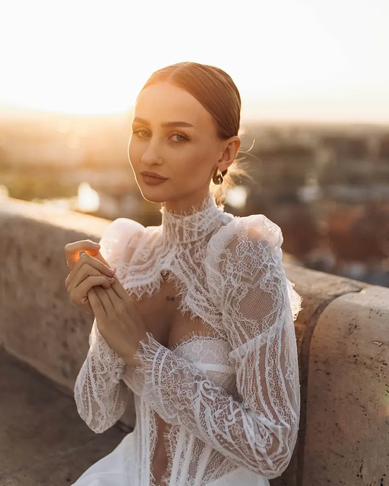 Woman in a white lace blouse on Fisherman's Bastion at sunset, looking at the camera, with the Budapest skyline glowing behind her.